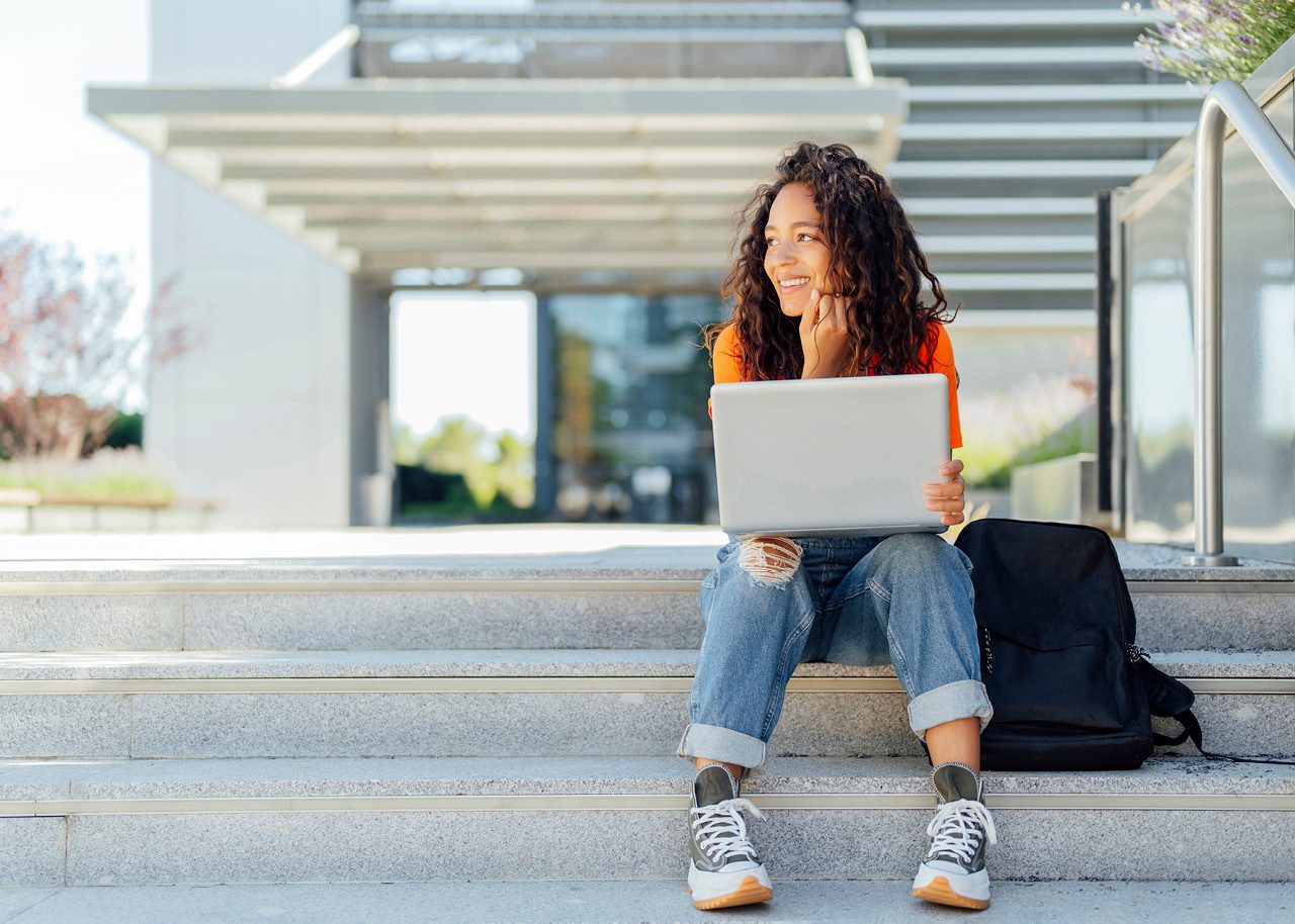 Image of female college student with laptop sitting on campus stairs outside